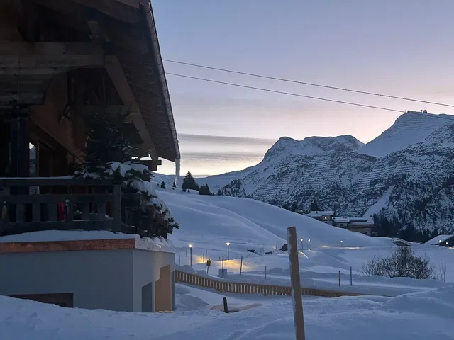 Schneebedecktes Chalet am Hang, Berge im Hintergrund bei Sonnenuntergang